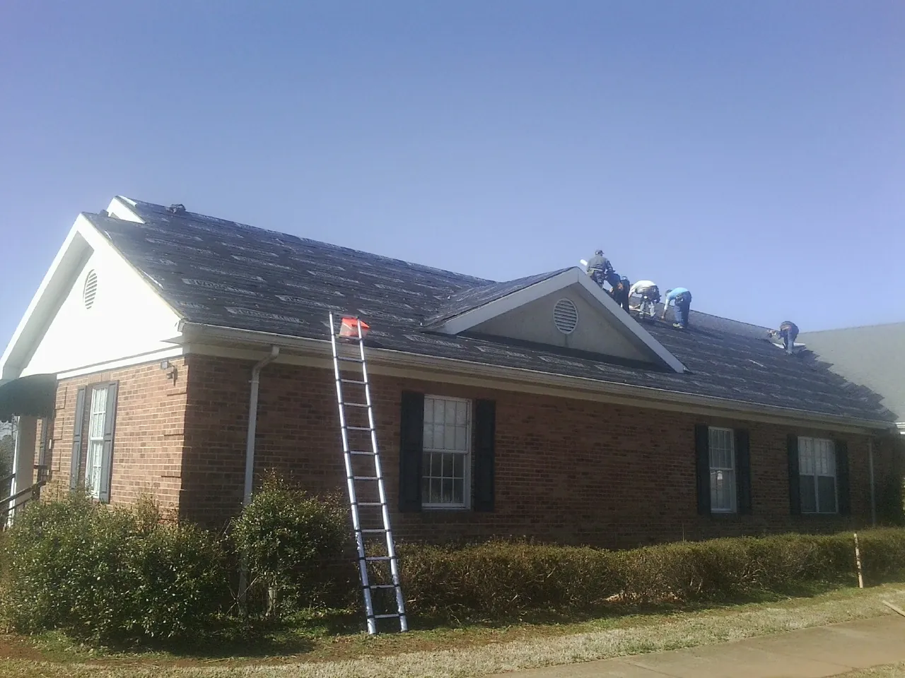 Crew tearing shingles off a brick ranch roof with a ladder set — Emergency Roof Repair work by our crew in Centerburg