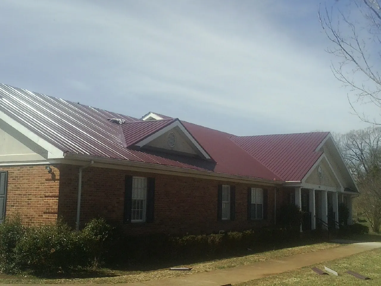Red metal roof with gabled entries on a long brick building, from a Hail Damage Roof Repair job in Centerburg