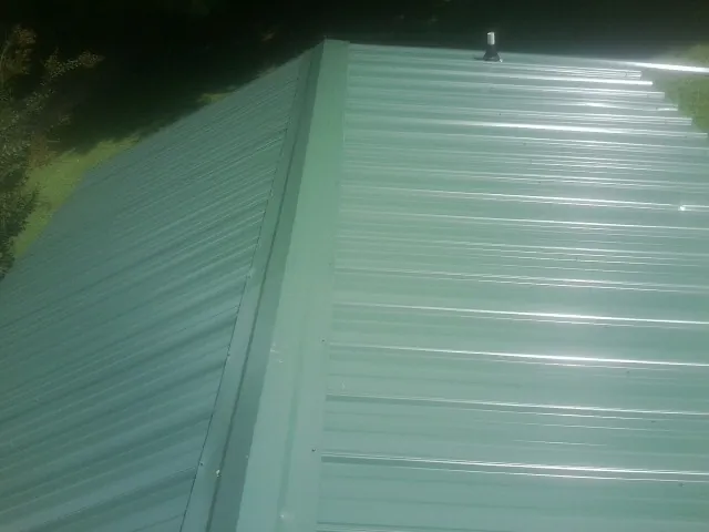 New green metal panels meeting at the ridge of a roof — Flat Roof Repair work by our crew in Centerburg