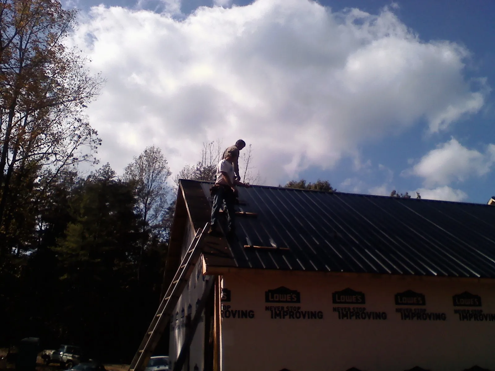 Roofer fastening dark metal panels high against a cloudy sky, from a Roof Inspection job in Centerburg