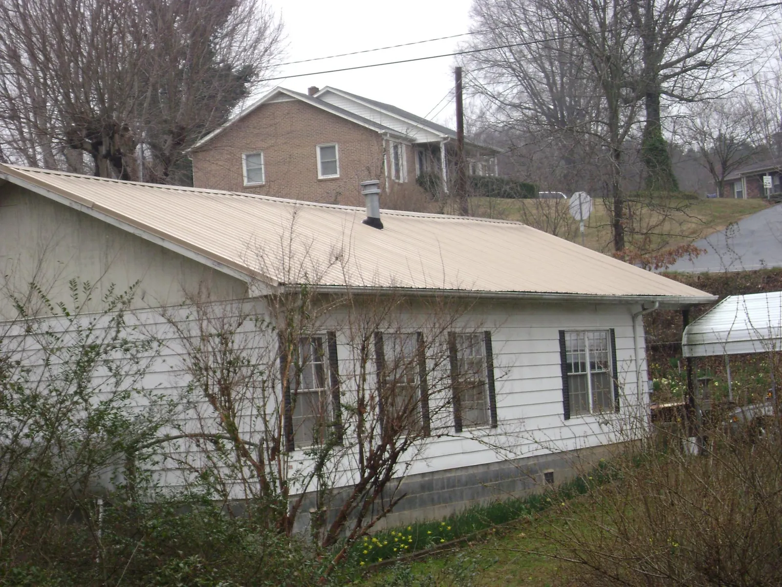 Tan metal roof on a white sided house set into a hillside — Commercial Roofing by Roofing Brothers in Centerburg